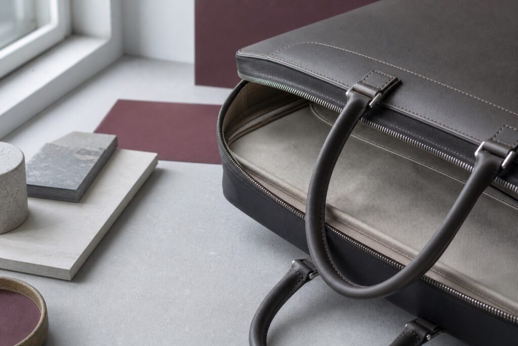 Dettagli ravvicinati di cuciture, bordo, fodera e chiusura osservati su una borsa neutra senza marchio.