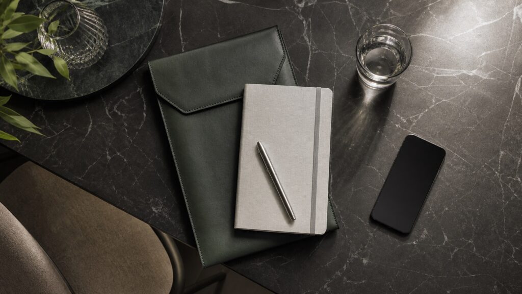 Flat lay editoriale di agenda, custodia e tecnologia in materiali diversi ma cromaticamente coerenti.